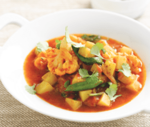 Bowl of vegetable and shrimp curry garnished with cilantro
