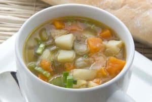 Bowl of vegetable soup with bread on white plate