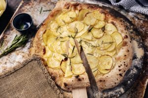 Rustic potato and rosemary pizza slice on wooden board