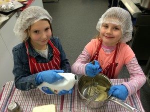 Two girls with hairnets and gloves mixing ingredients in bowl