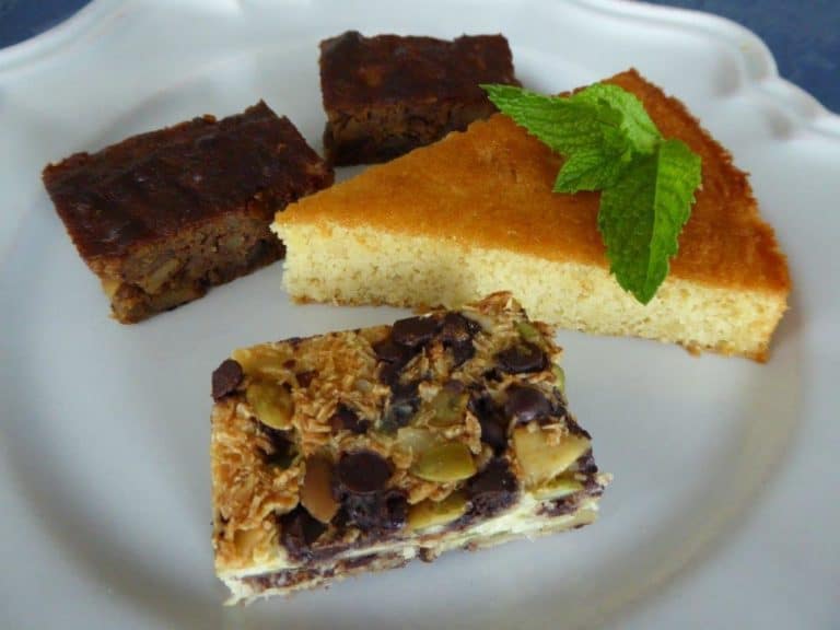 Assorted homemade dessert bars and cake slice on white plate.