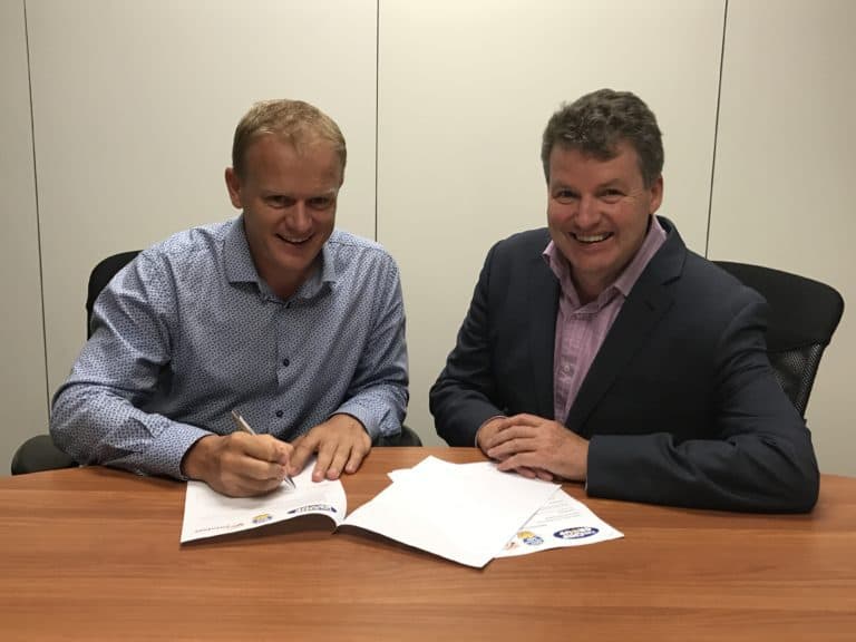 Two men signing documents at office table, smiling