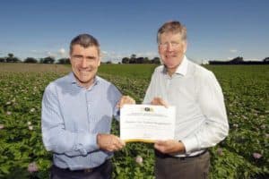 Two men holding certificate in green agricultural field outdoors