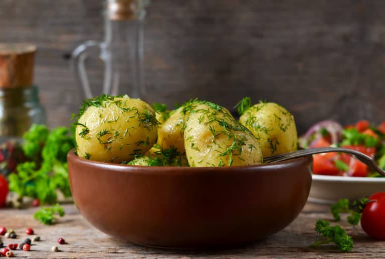 Young, boiled potatoes with butter and dill on a wooden background.