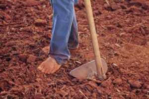 Barefoot person working with hoe tool on dry soil field