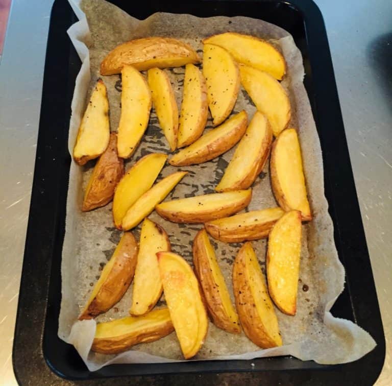 Baked seasoned potato wedges on parchment paper-lined tray
