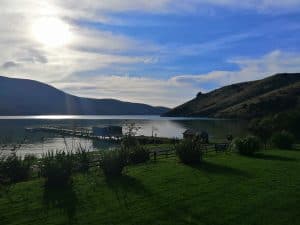 Serene lakeside with dock, hills, and bright sky sunlight