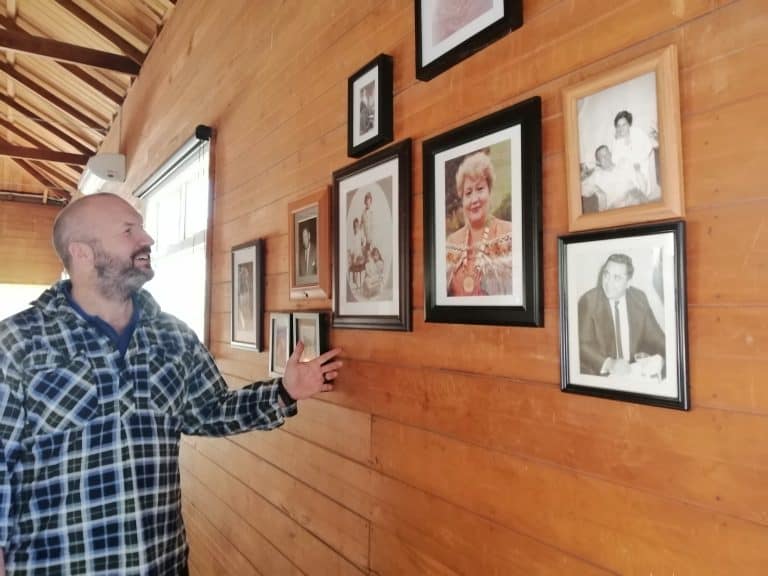Man in checkered shirt looking at framed family photos on wooden wall