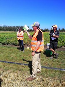 Farm workers in high-visibility vests discussing in green field
