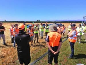 Group of people in safety vests gathered in agricultural field meeting