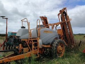 Jacto agricultural sprayer machine in a grassy field under cloudy sky.