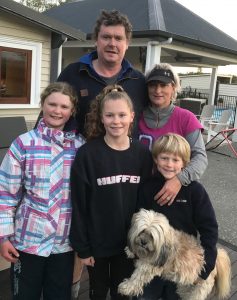 Family of five with a dog posing outside a house.