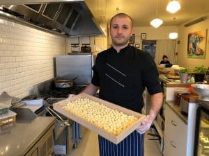 Chef holding wooden tray of fresh gnocchi in professional kitchen