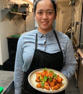 Chef holding plate of spicy cooked sweet potatoes garnished with herbs