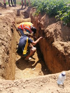 Two workers examining soil layers in deep trench outdoors