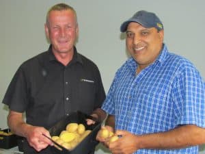 Two men smiling holding fresh potatoes in container and hands