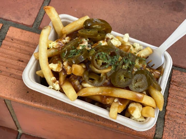 Poutine with jalapeños and gravy in a takeout container.
