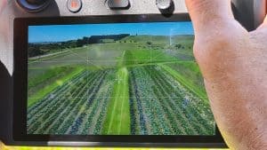 Drone controller screen showing aerial view of green farmland fields.