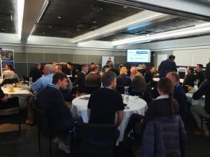 Business conference attendees seated at round tables listening to speaker