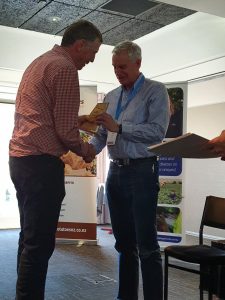 Two men shaking hands during award presentation ceremony indoors.