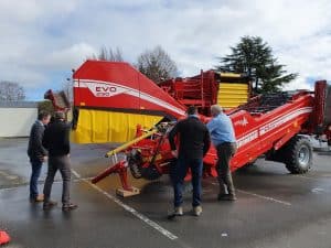Four men inspecting large red Grimme agricultural machinery outdoors