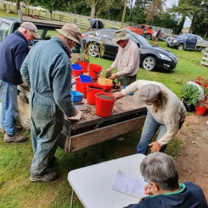 Group of people outdoors sorting soil samples into red buckets on truck bed