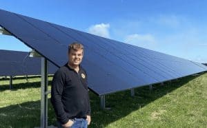 Man standing beside large solar panel array on sunny day