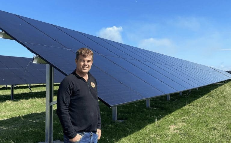 Man standing beside large solar panel array on sunny day