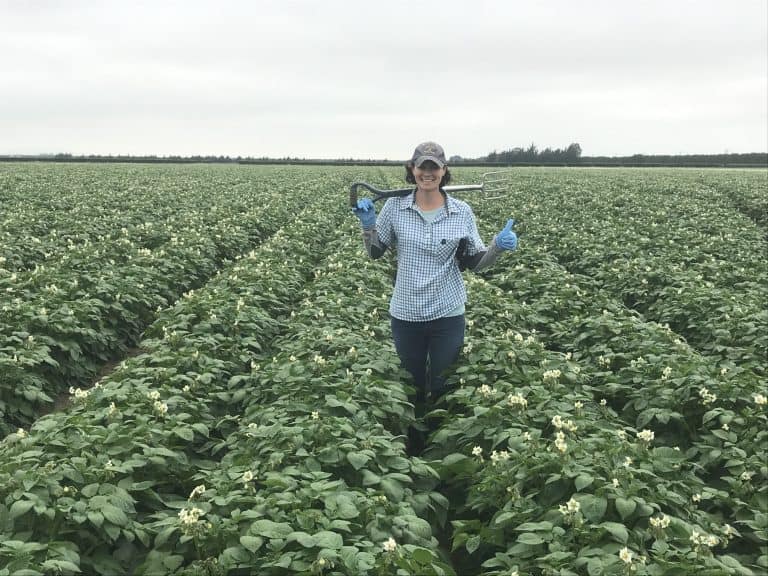 Woman in plaid shirt holding garden fork in potato field