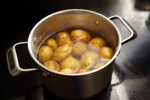 Potatoes with peel in a stainless steel pot with boiling water on the stove, healthy cooking concept, copy space, selected focus