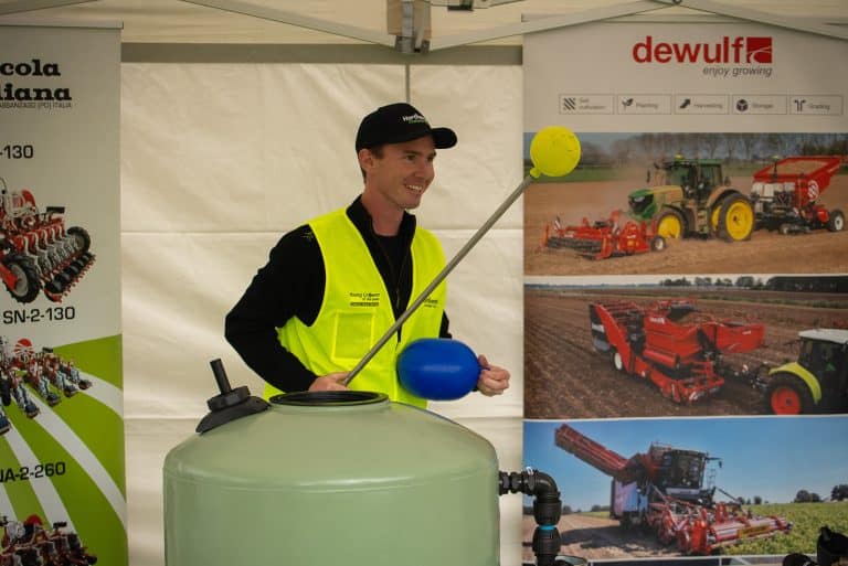 Man in safety vest demonstrating agricultural equipment at exhibition booth.