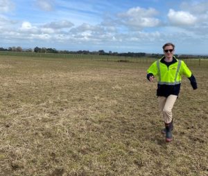 Man in high-visibility jacket walking across open farmland field