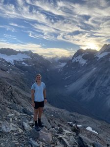 Person standing on rocky mountain with snowy peaks and dramatic sky background
