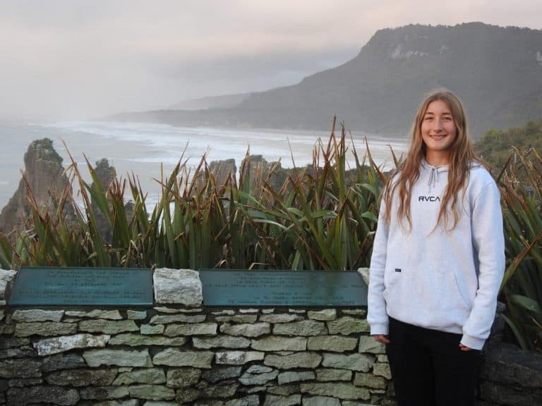 Young woman in hoodie smiling with coastal cliffs and mountains background