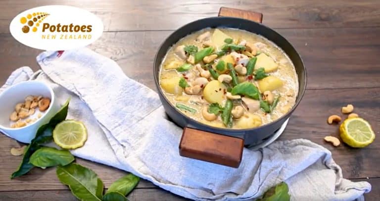 Potato and cashew curry garnished with herbs in black pan
