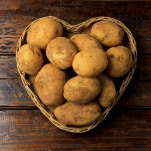 pile of fresh and raw potatoes harvested from plantation and placed in heart shaped wicker basket on wooden table. Top view.
