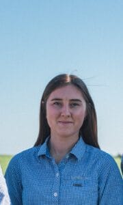 Young woman in blue checkered shirt standing outdoors.