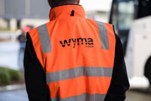 Person wearing orange high-visibility WYMA safety vest with reflective stripes.