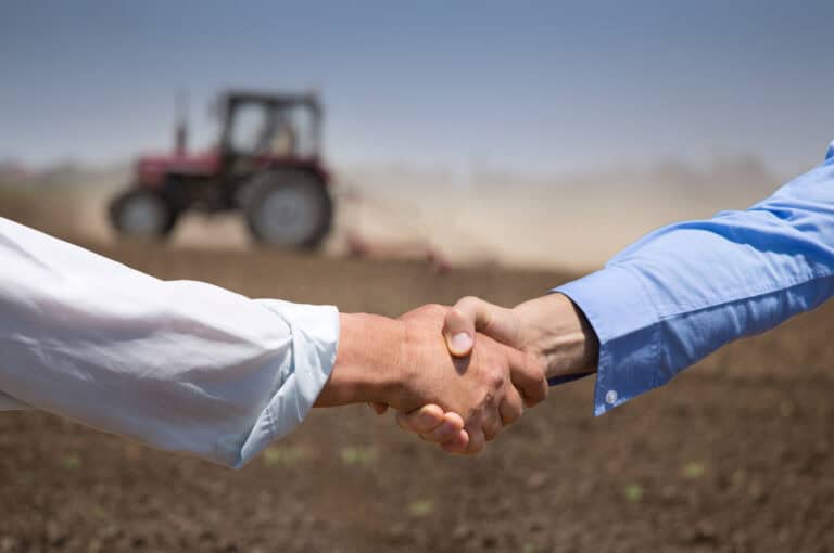 Farmers shaking hands with tractor working in background