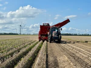 Tractor harvesting crops in agricultural field with wind turbines.