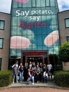 Group of people posing outside Agrico building with potato advertisement.