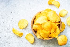 Potato chips in wooden bowl on white table. Top view.