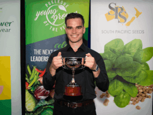 Man holding Pukekohe Young Grower of the Year trophy smiling.
