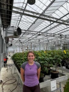 Young woman standing inside a greenhouse with potted plants.