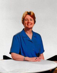 Middle-aged woman smiling, wearing blue shirt, seated at round table