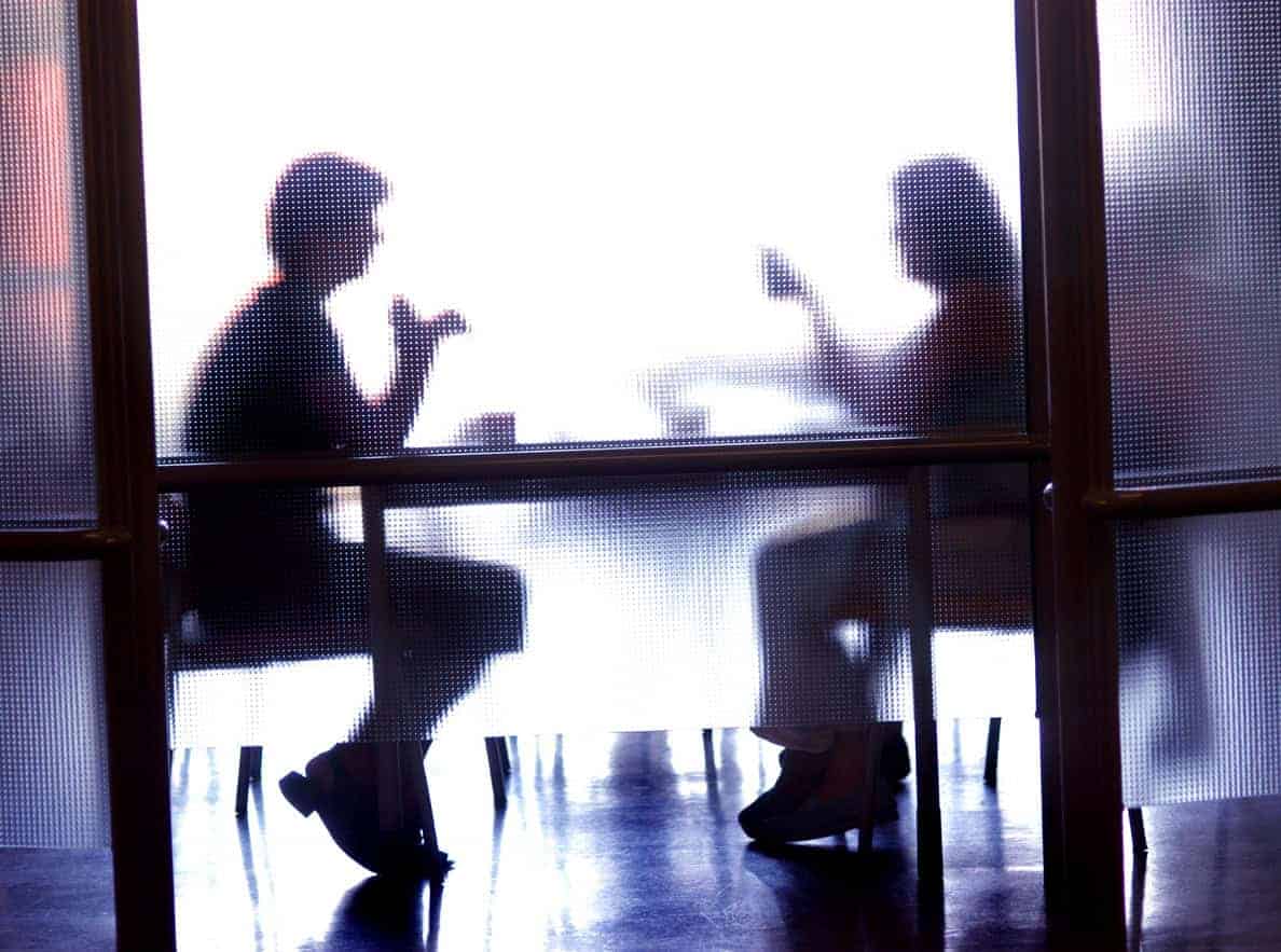 Silhouettes of two people sitting and drinking behind frosted glass.